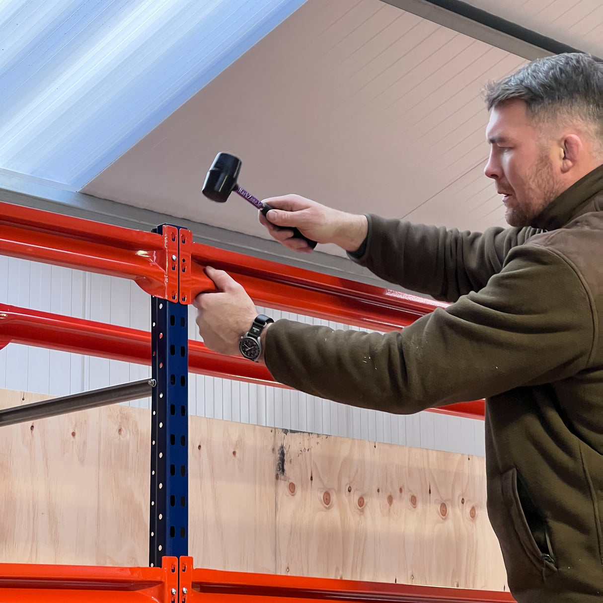 Man assembling RackZone Longspan Shelving 400mm Starter with mallet indoors.