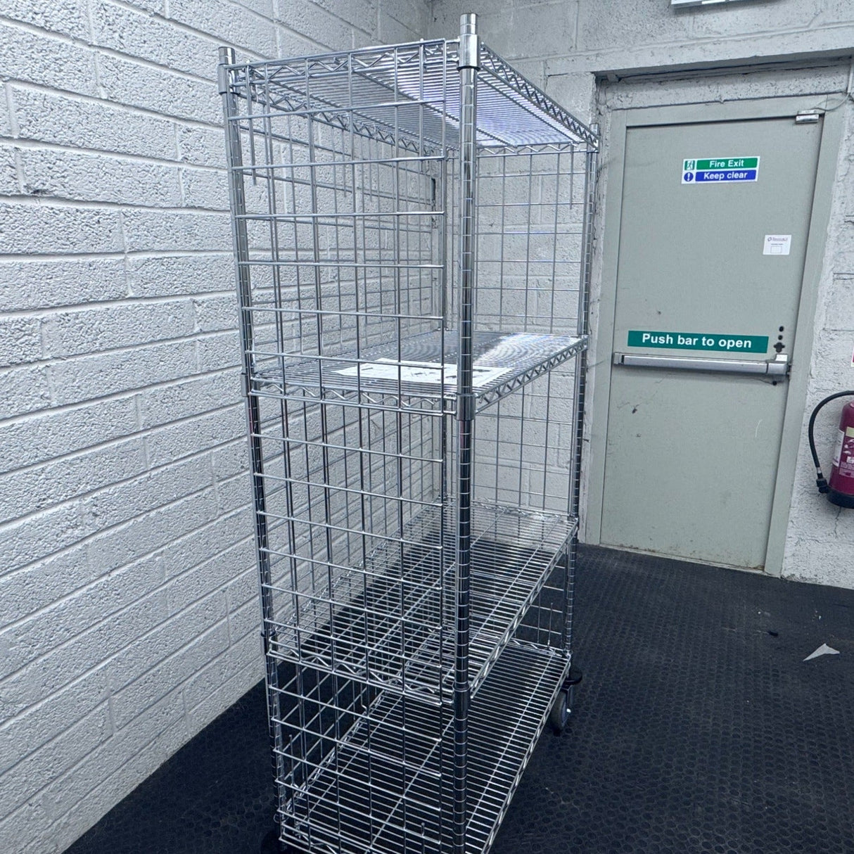 A RackZone 4 Tier Chrome Trolley stands near a gray emergency exit door.