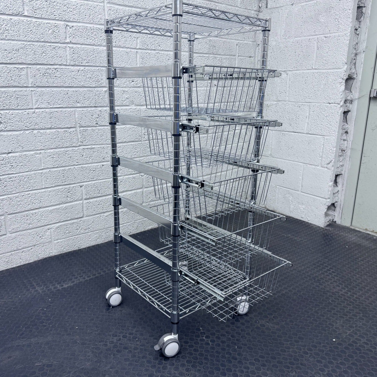 RackZone 5 Tier Chrome Plated Basket Trolley stores items by a gray brick wall.