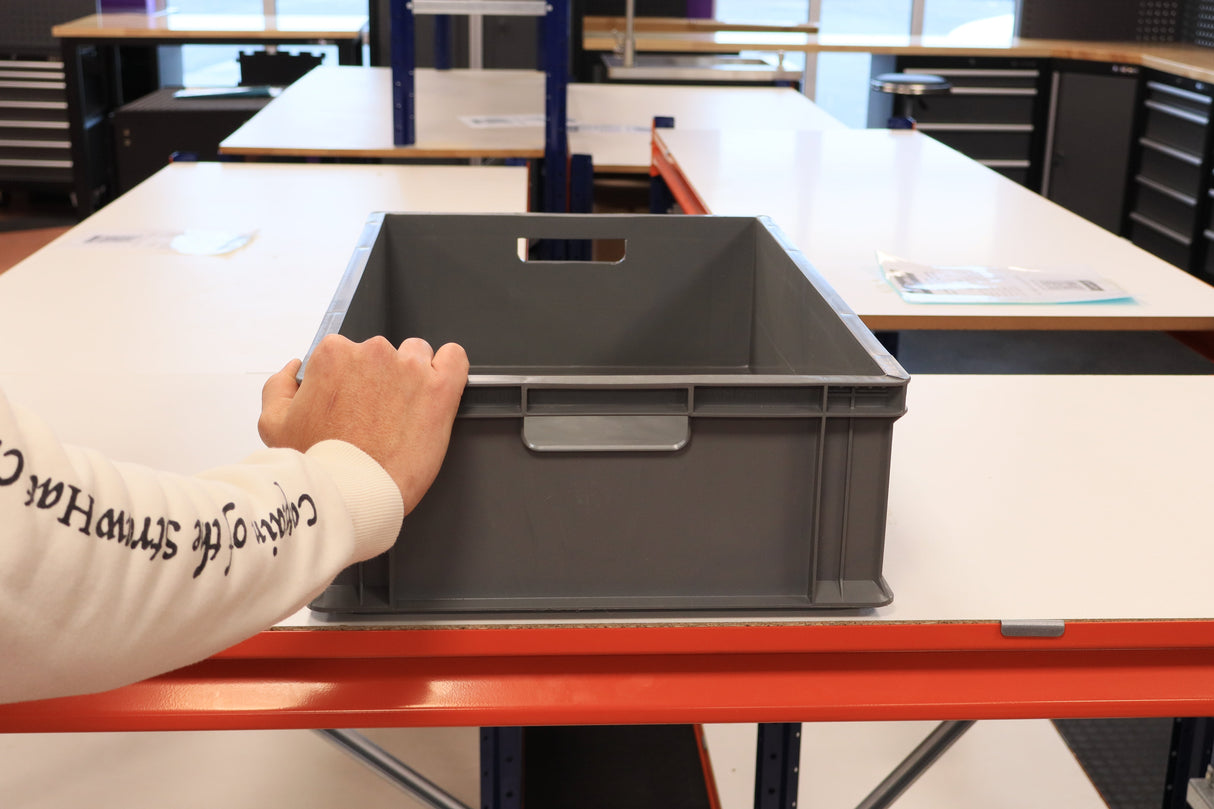 Someone places a RackZone 65 Euro Container (grey) on a white table in a workshop.