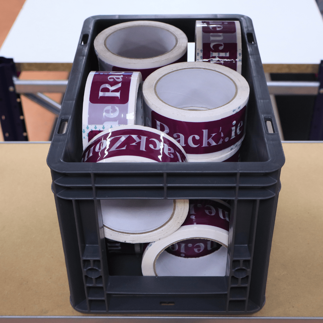 A RackZone Euro Picking Container holds packing tape rolls on a table.