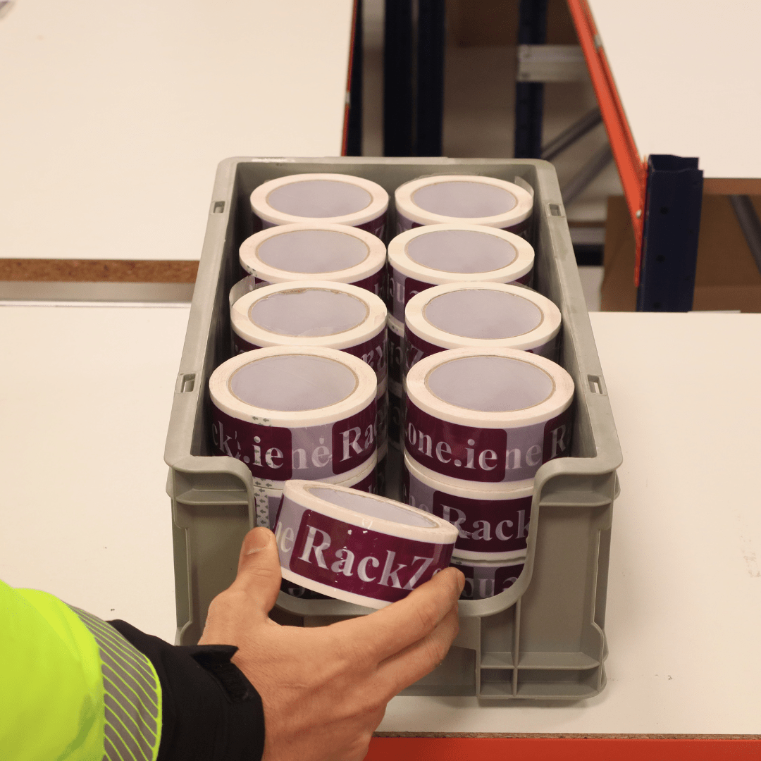 A hand holds a RackZone Euro Picking Container 505d filled with purple labels.
