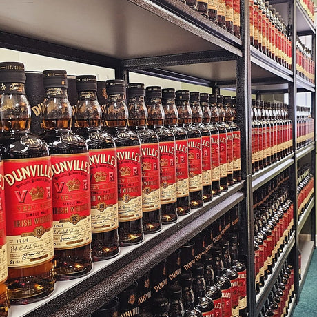 Shelves stocked with multiple rows of Dunville's Irish Whiskey bottles, all labels facing forward in a liquor store or storage setting.