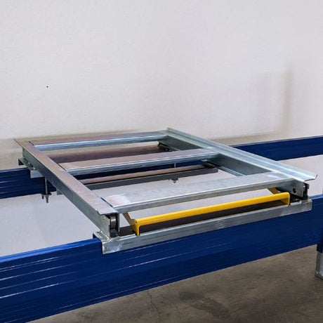 A metal frame with a yellow plastic component is mounted on blue rails, positioned above a concrete floor against a plain wall.