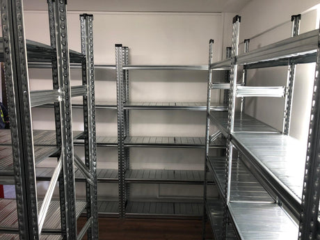 Empty metal shelving units are arranged along the walls in a small room with a wooden floor.