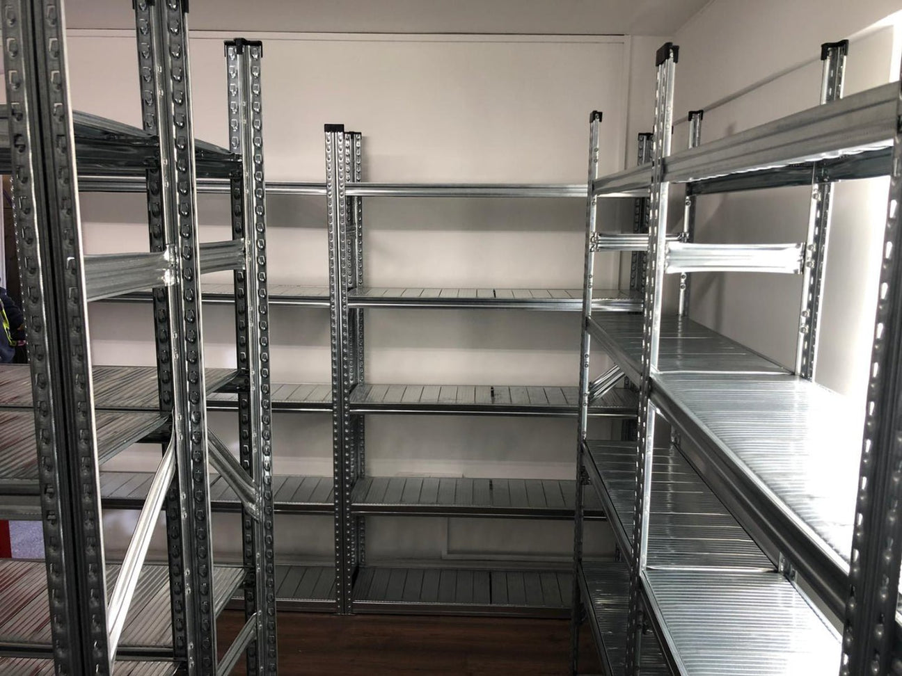 Empty metal shelving units are arranged along the walls in a small room with a wooden floor.