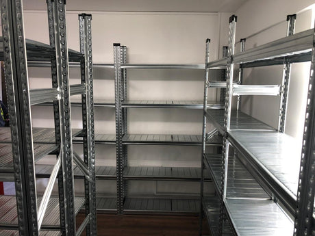 Empty metal shelving units are arranged along the walls in a small room with a wooden floor.