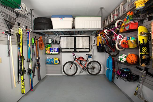 Organized garage with sports equipment, including skis, a bicycle, skateboards, balls, tools, and various items stored on shelves and hanging racks.