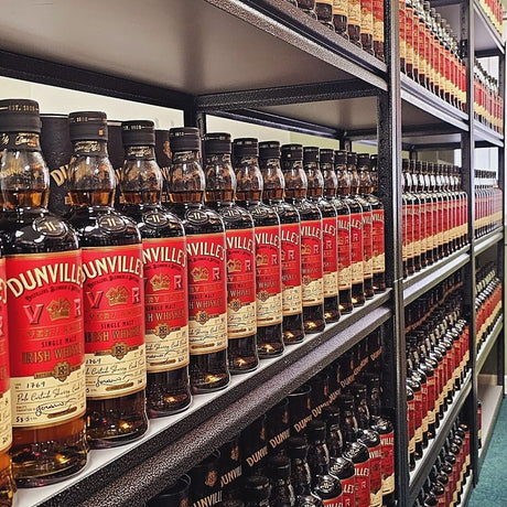 Shelves stocked with multiple rows of Dunville's Irish Whiskey bottles, all labels facing forward in a liquor store or storage setting.