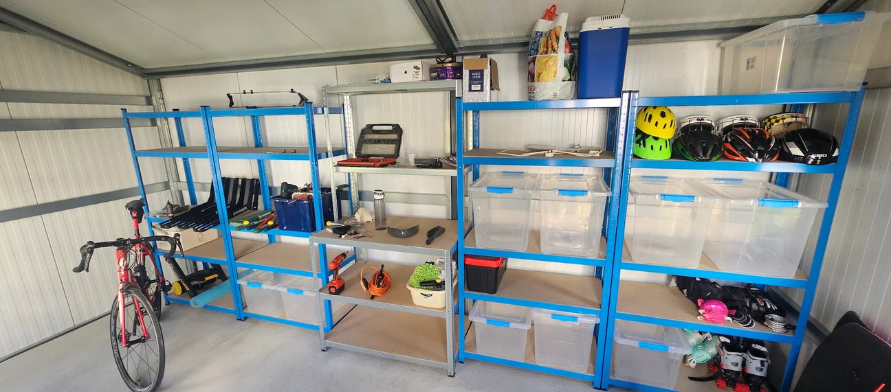 Organized metal shelves in a garage hold cycling gear, helmets, tools, and storage bins. A road bicycle is parked on the left side of the image.
