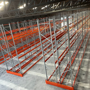Pallet rack system in a warehouse setting with concrete flooring and metal beams.