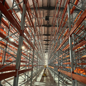 High-rack warehouse with red shelves and a central aisle.