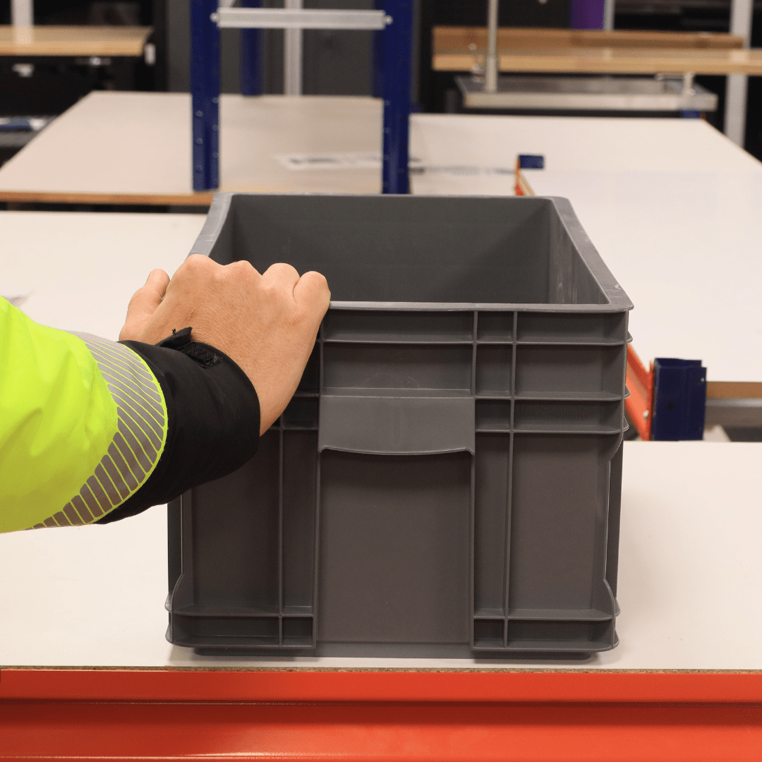 A hand holding a RackZone Euro Container 505x295x235mm Grey on a table.
