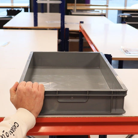 Someone places RackZone Euro Container 600x400x100mm Grey on a white table.