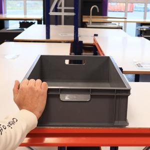 A person places a RackZone Euro Container 600x400x150mm Grey on a table.