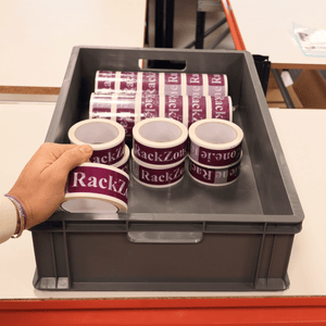A hand holds RackZone tape above Euro Container 600x400x150mm Grey crates.