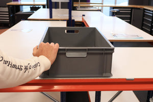 Someone places a RackZone 65 Euro Container (grey) on a white table in a workshop.