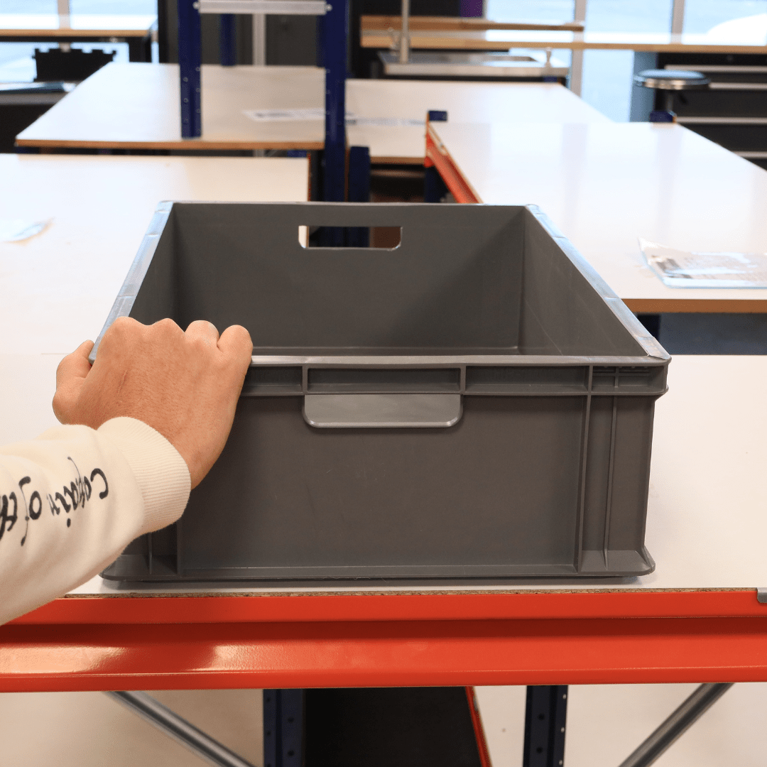 A hand holds a RackZone Euro Container 600x400x175 on a white and orange table.