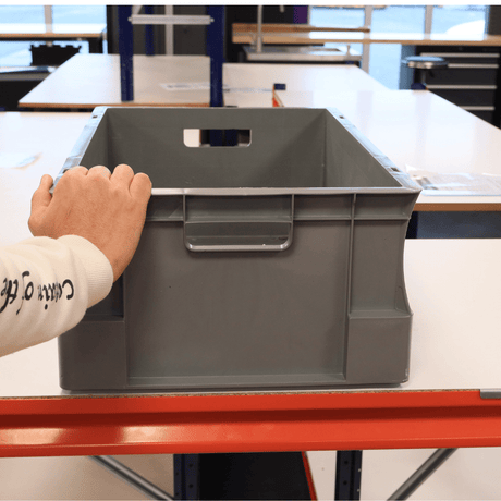 A person sets a RackZone Euro Container 600x400x230mm Grey on a table.