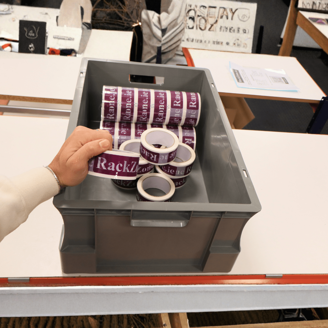 A hand holds a RackZone Euro Container 600x400x230mm filled with tape rolls.