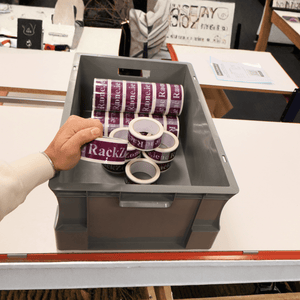 A hand holds a RackZone Euro Container 600x400x230mm filled with tape rolls.