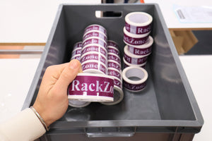 A hand holds RackZone tape in a bin of 45 RackZone Euro Containers, grey.