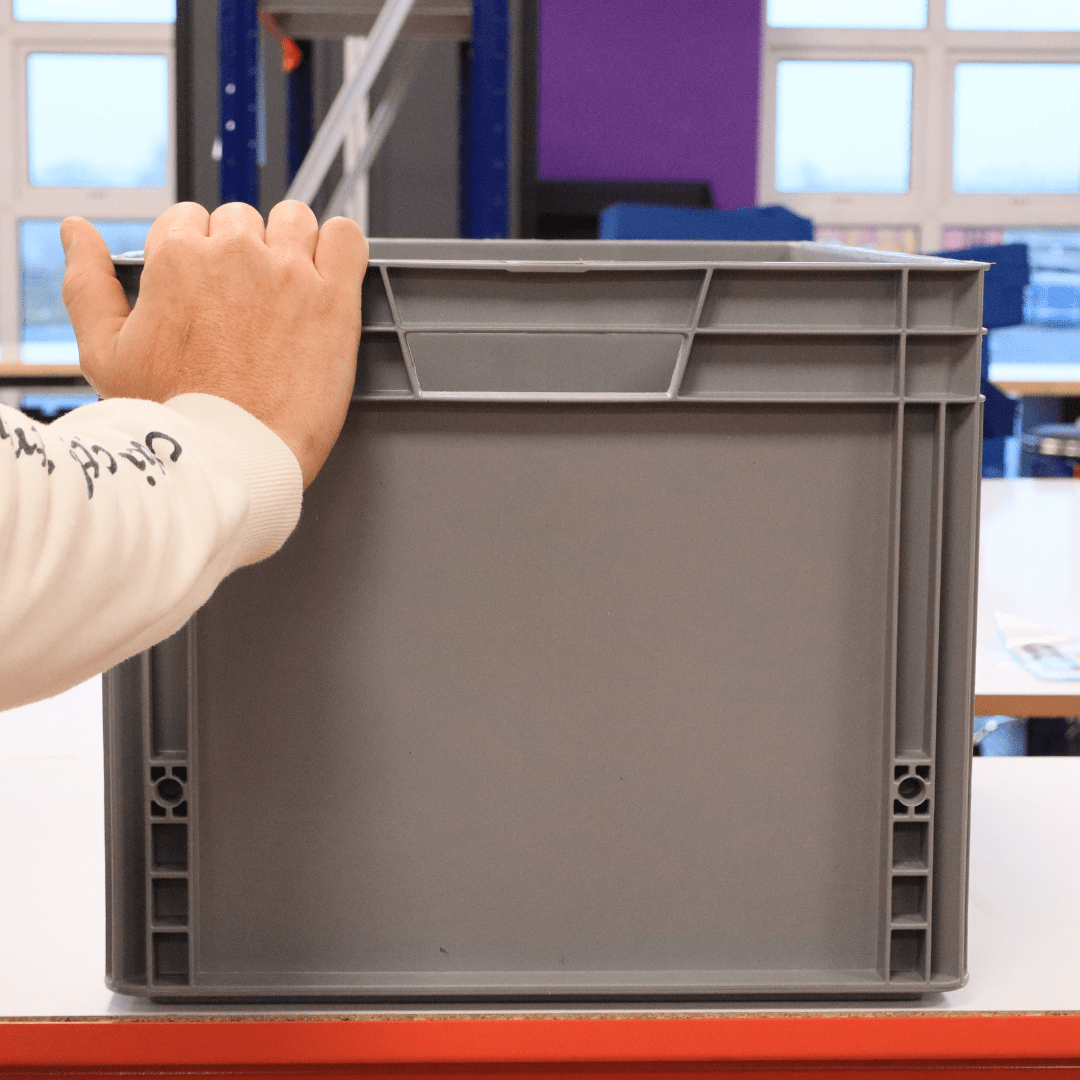 A hand holds a RackZone Euro Container 600x400x340mm Grey on a table.
