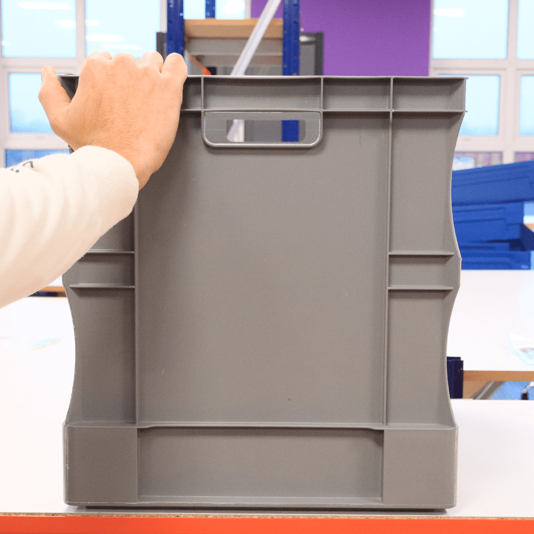 A hand holds a RackZone Euro Container 600x400x420mm Grey on a white table.
