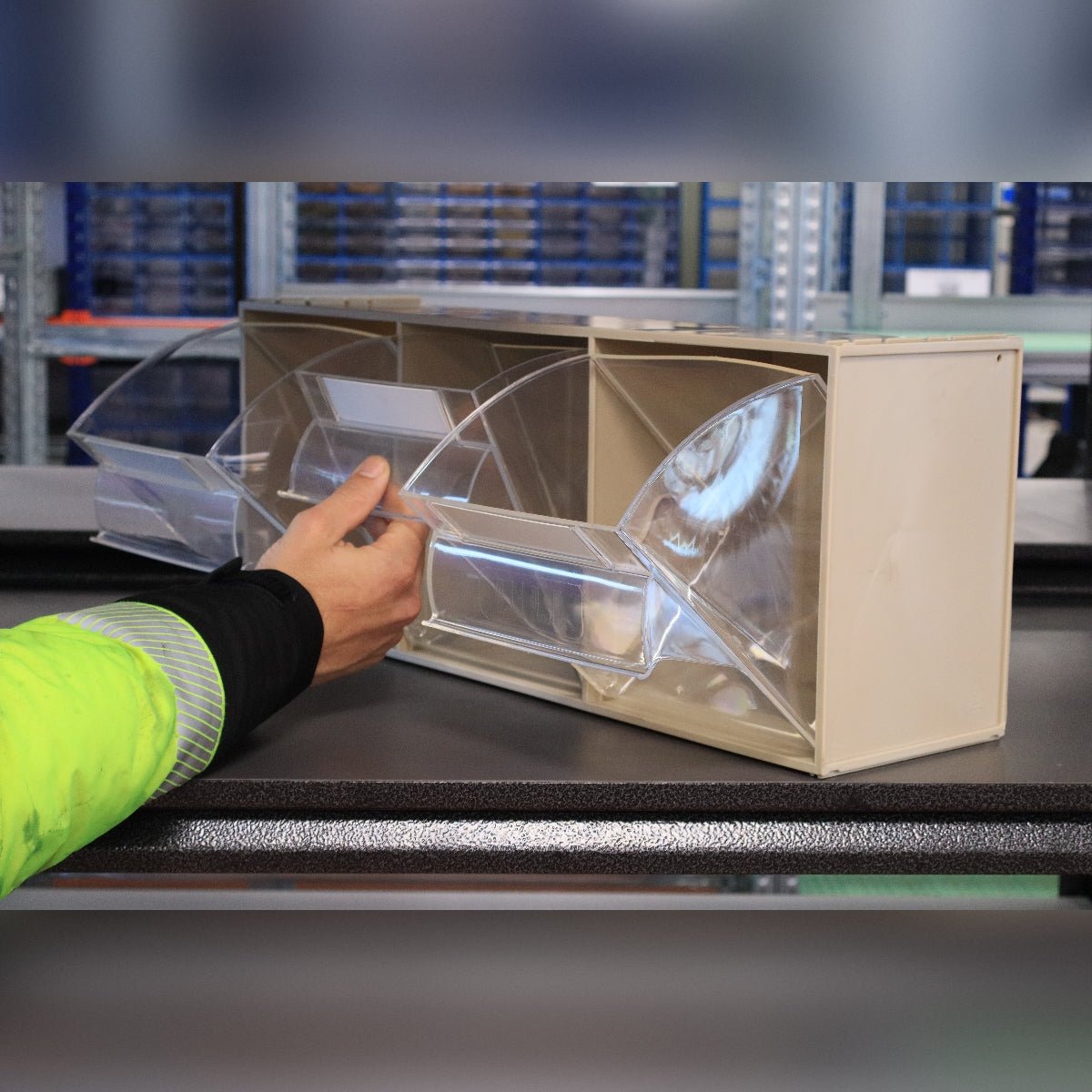 Someone opens a RackZone Tilt Bin Madia 5 on a beige storage unit in a warehouse.