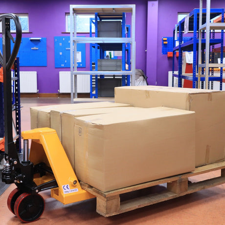 The RackZone Pallet Truck 2500kg with PU wheels moves boxes in a purple warehouse.