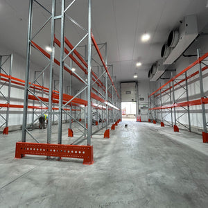 Empty warehouse with metal shelving units and red safety barriers.
