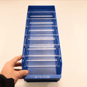 A hand holds a blue RackZone ST5018-11 shelf bin with multiple compartments.