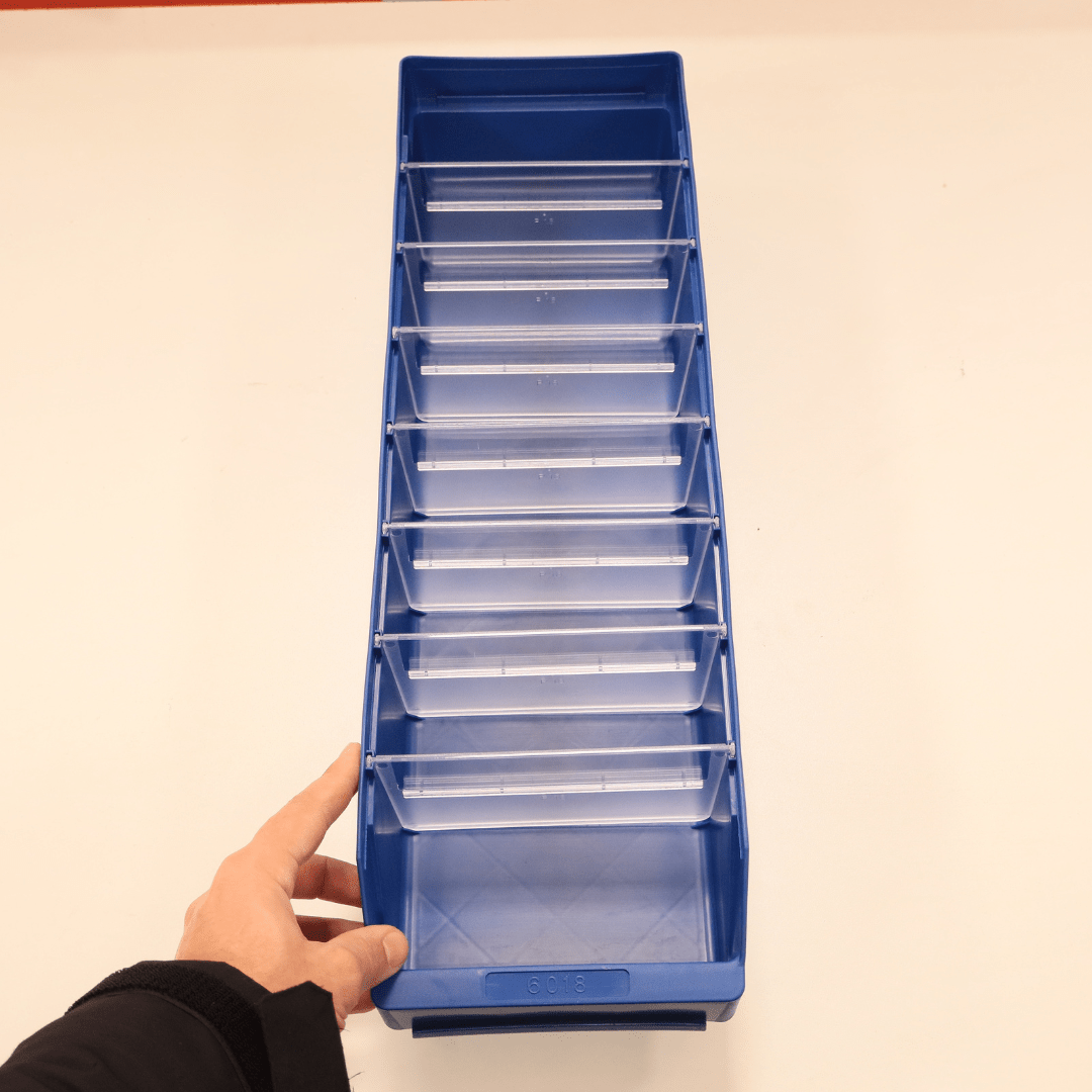 A hand holds a RackZone ST6018 blue shelf bin with eight clear dividers.
